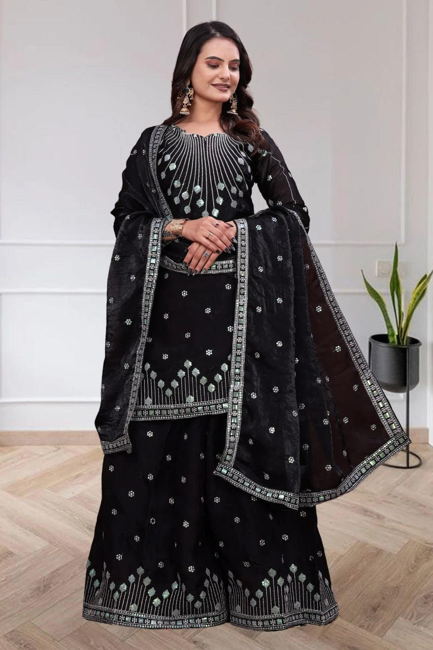 Woman wearing a black traditional outfit with intricate designs indoors.